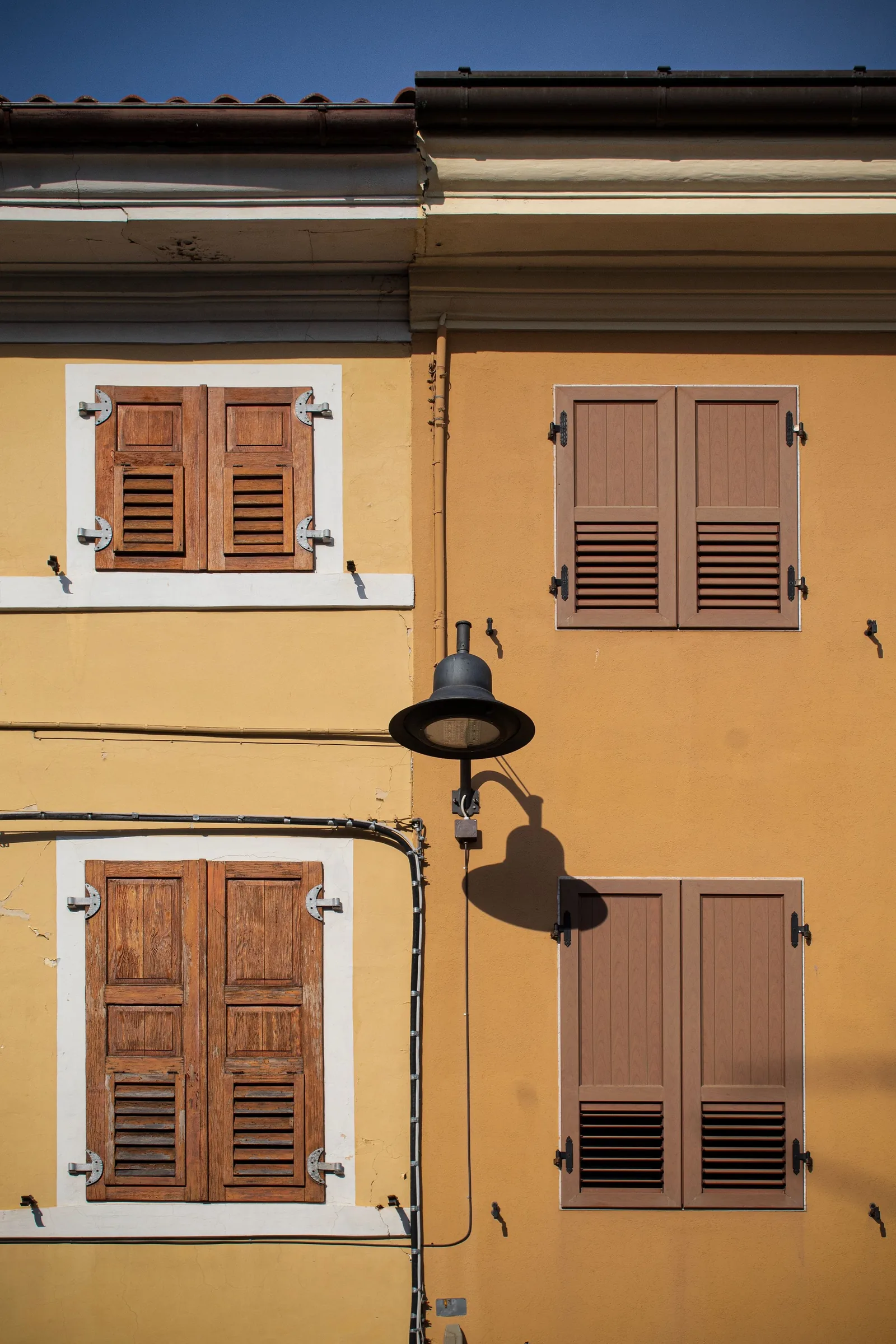 Ochre wall with brown shutters and a lamp